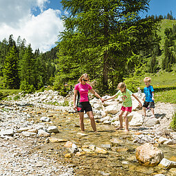 AllesAlm Eine Familie steht in einem kleinen Bach