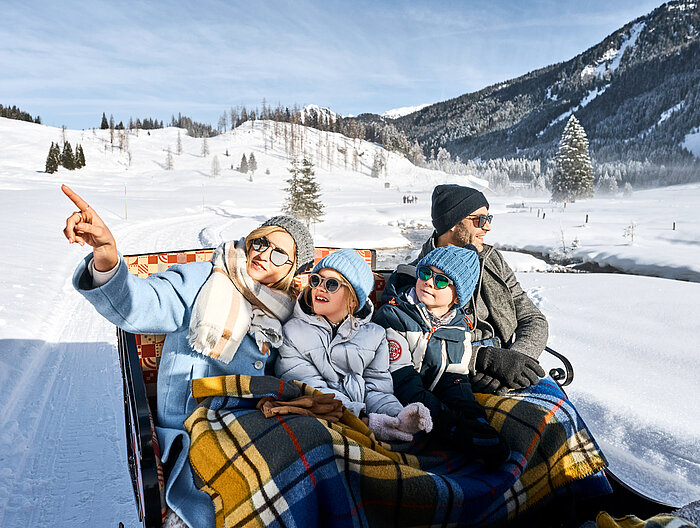 Mehrere Personen fahren mit einem Pferdeschlitten über die winterliche Landschaft
