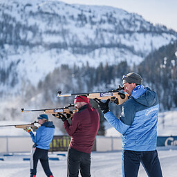 Drei Personen beim Zielen mit einer Biathlonwaffer vor der Gnadenalm