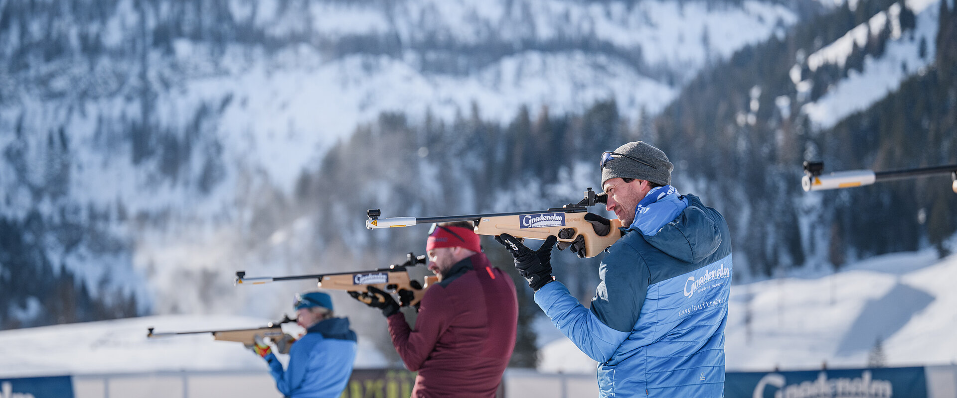 Drei Personen beim Zielen mit einer Biathlonwaffer vor der Gnadenalm