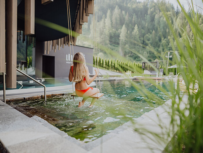Eine Frau schaukelt über den Naturpool im Adults Only Bereich des Wellnesshotels Lürzerhof in Salzburg